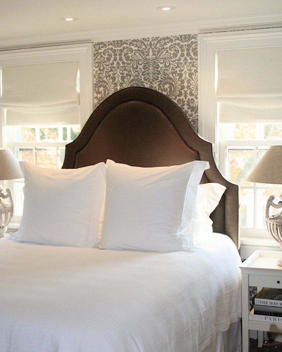 Bed with a dark arched headboard against a patterned wallpaper
