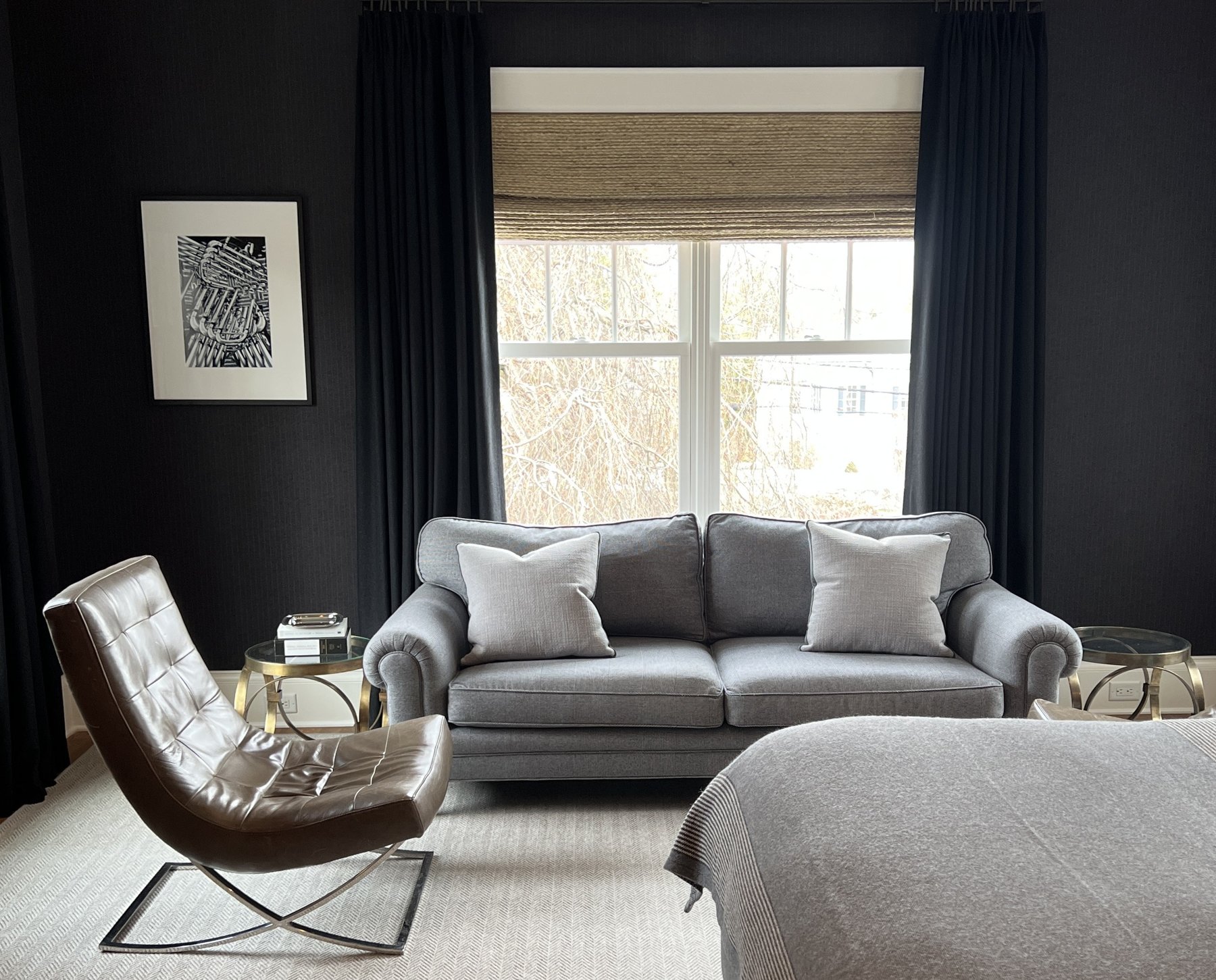 Bedroom sitting area with a grey sofa and a leather sling chair against dark walls