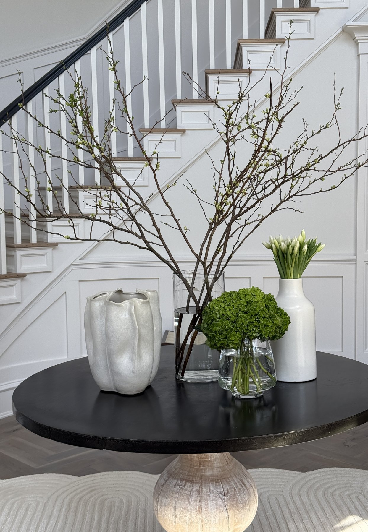 Entry hall with a round black table, spring branches and a panelled staircase