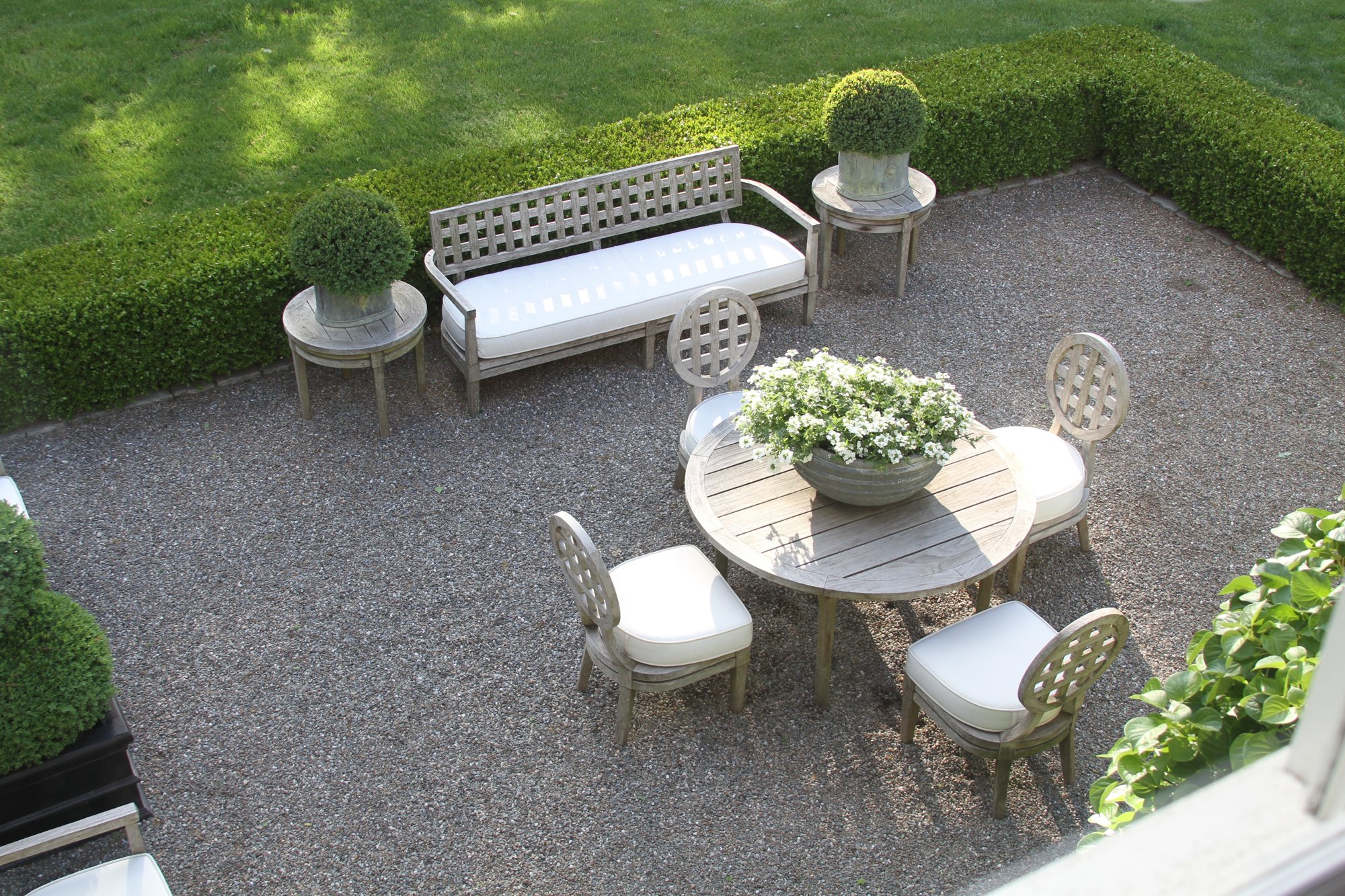 Gravel garden terrace edged in boxwood, with teak seating and topiary