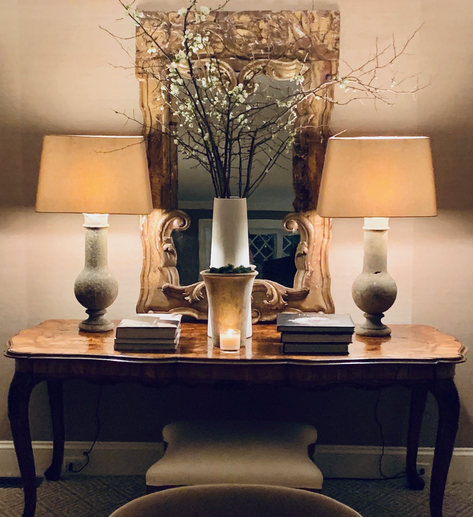 Console table at night with paired lamps, a gilt mirror and spring branches