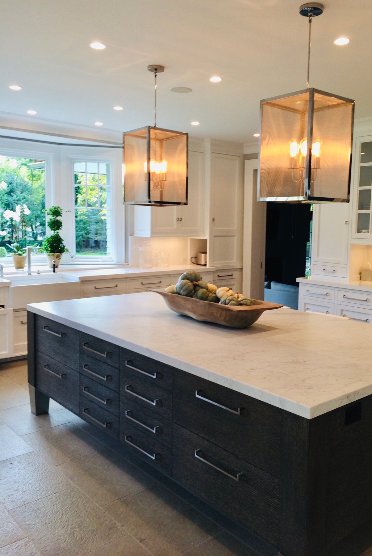 Kitchen with white cabinetry, a dark oak island under marble, and mesh lantern pendants
