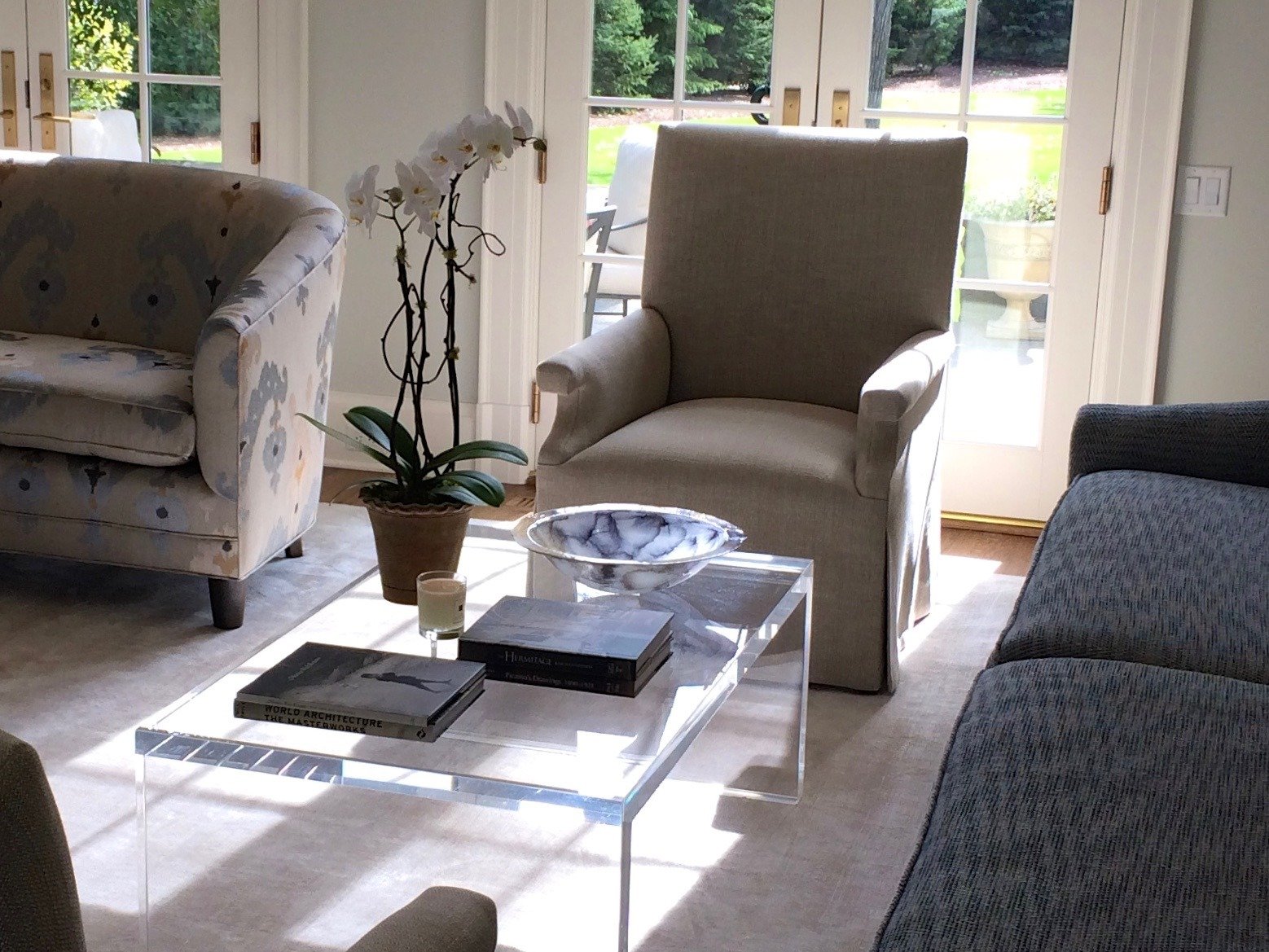 Living room with patterned slipper chairs, a lucite table and french doors to the garden