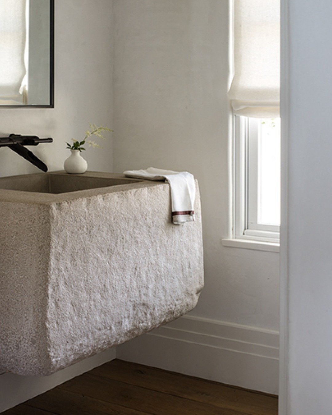 Carved stone trough sink beneath a window with a linen shade