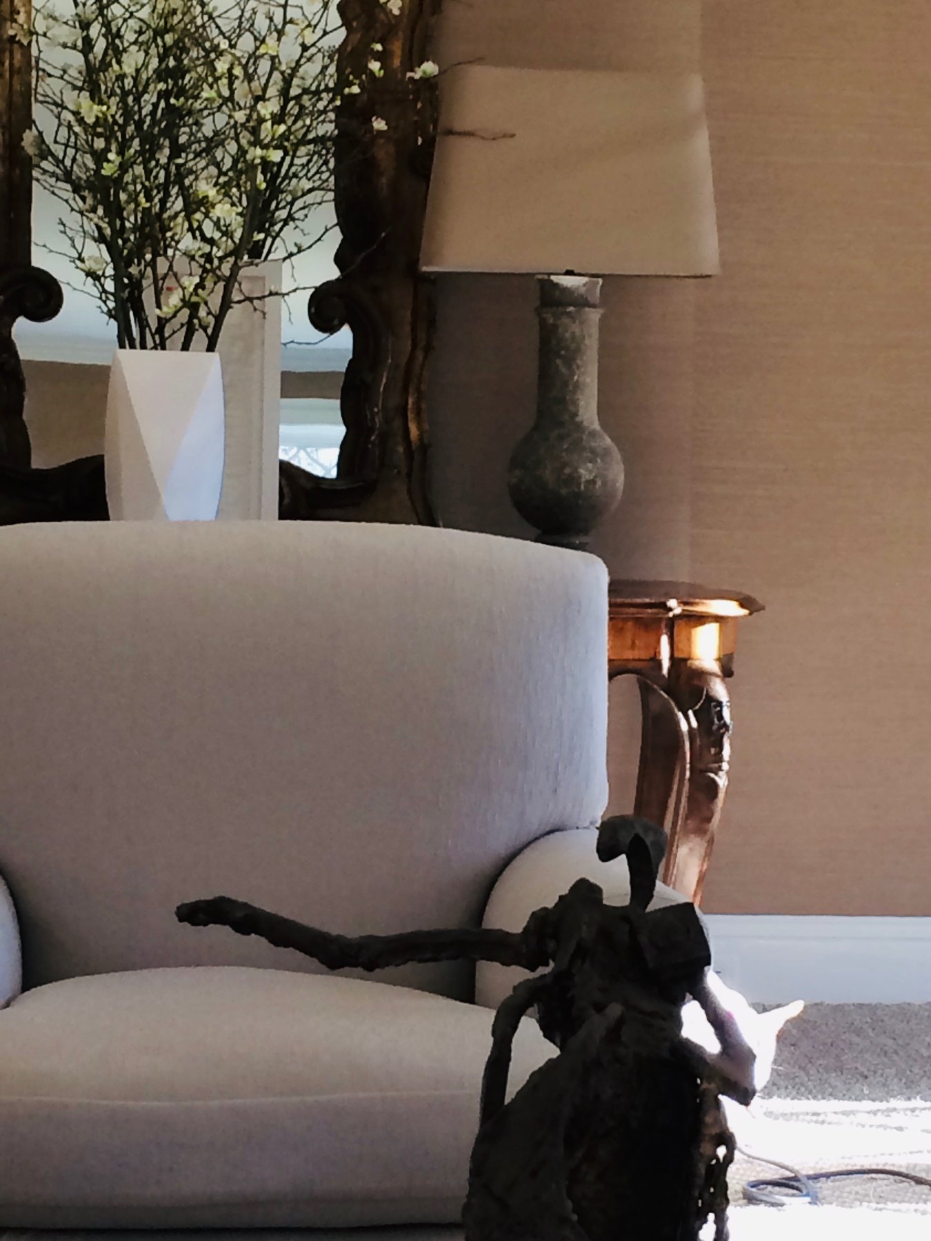 Armchair before a gilt mirror and grasscloth wall, with a stone lamp