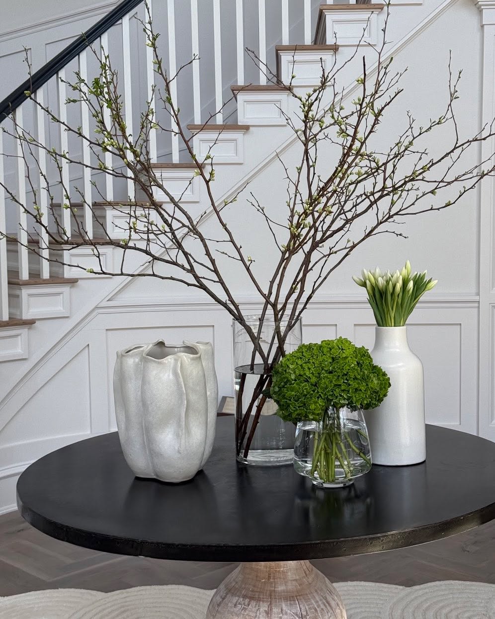 Entry table with branches and vases beside a panelled staircase